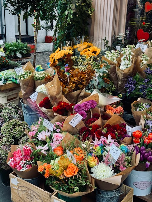 An outdoor display of various freshly cut floral arrangements, featuring a vibrant mix of flowers including bright yellow sunflowers, pink lilies, red and purple carnations, white and orange roses, an